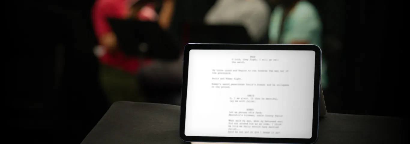 iPad with a blurred play script and three figures blurred in background
