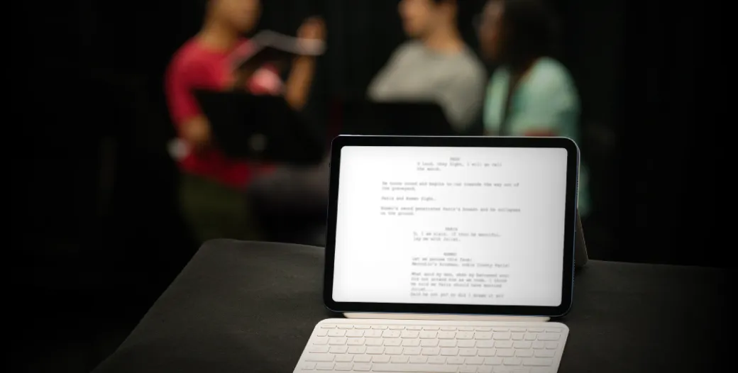 iPad with a blurred play script and three figures blurred in background
