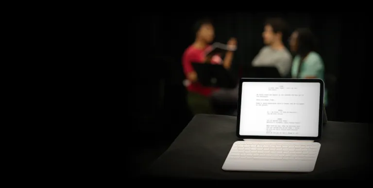 iPad with a blurred play script and three figures blurred in background