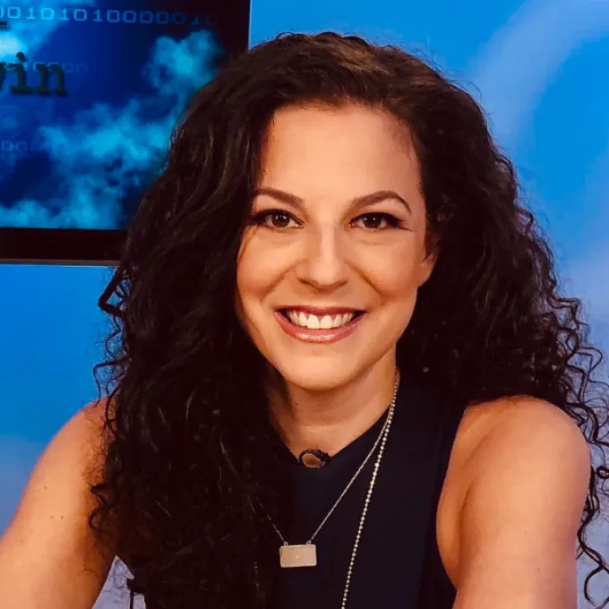 White woman with curly brown hair in front of a blue background