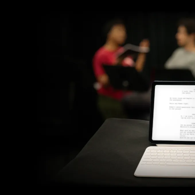 iPad with a blurred play script and three figures blurred in background