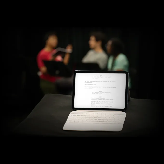 iPad with a blurred play script and three figures blurred in background